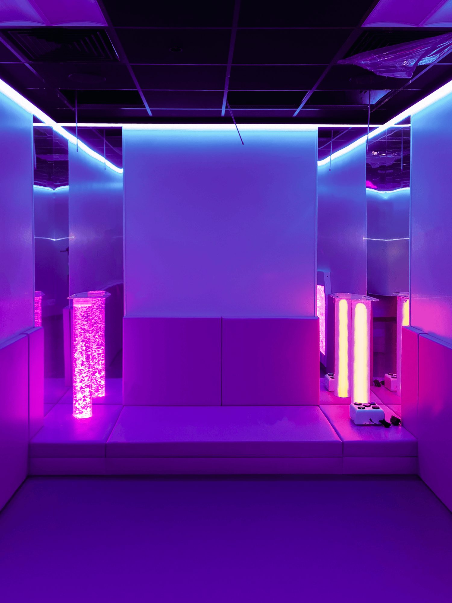 Mirrored futuristic room bathed in purple and blue neon, with a central screen, glowing light columns, and steps creating an immersive mood.
