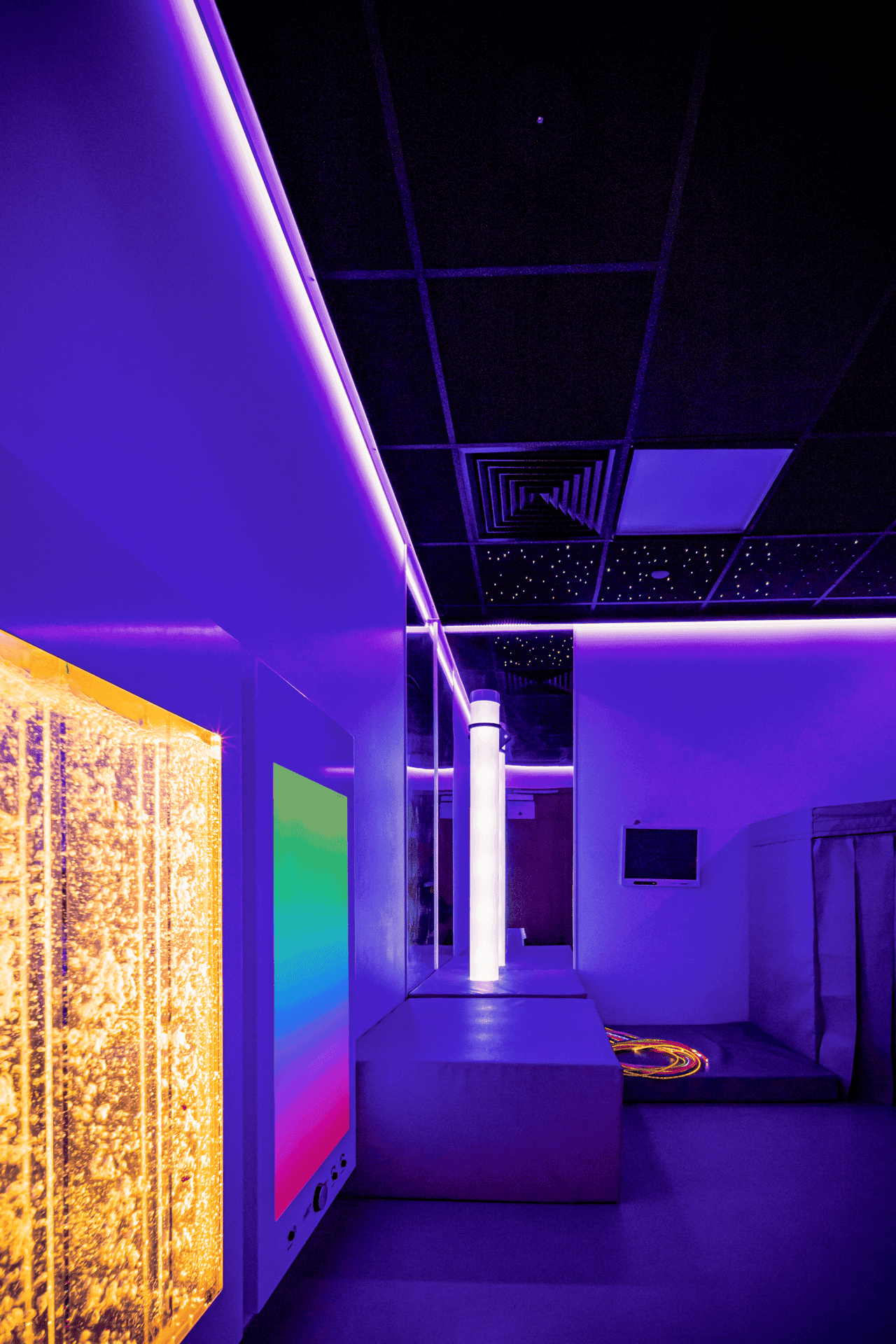 A sensory room with calming purple lighting, bubble tubes, and a colour-changing panel. The ceiling has a starry sky effect, creating a soothing atmosphere.