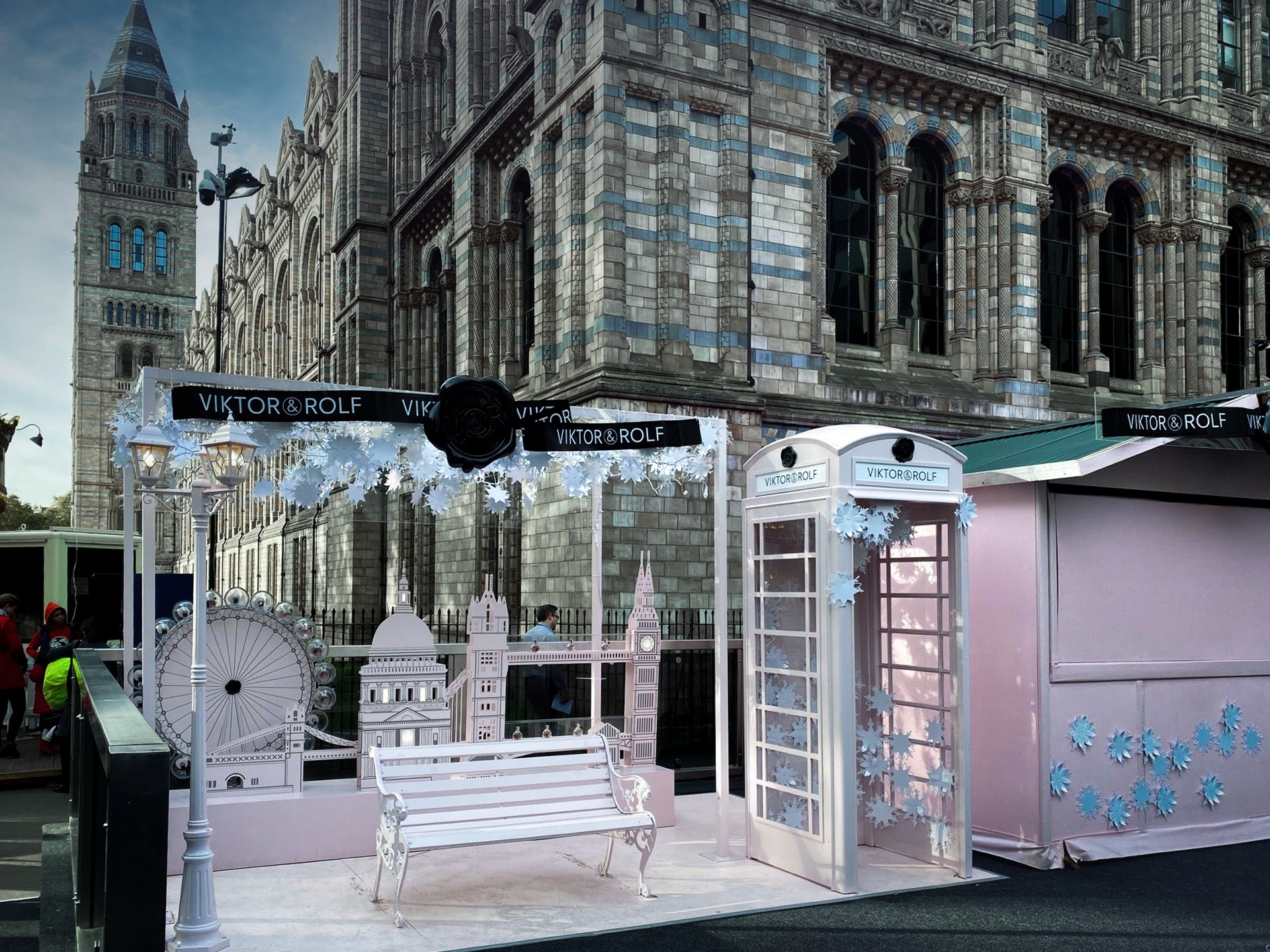 Festive Viktor & Rolf display featuring a white telephone booth, bench, and paper cutouts of London landmarks. Set against a historic building facade.