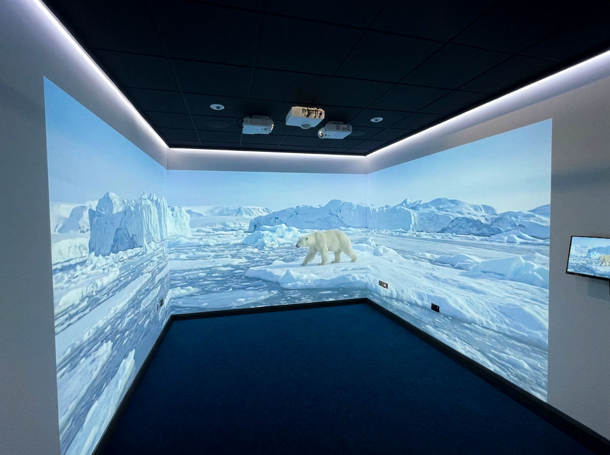 Immersive projection room shows a polar bear crossing a frozen Arctic landscape of blue ice, glaciers, and snowy mountains, creating a serene mood.