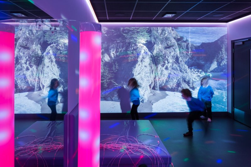 Children inside a sensory room with immersive visuals projected onto one wall.