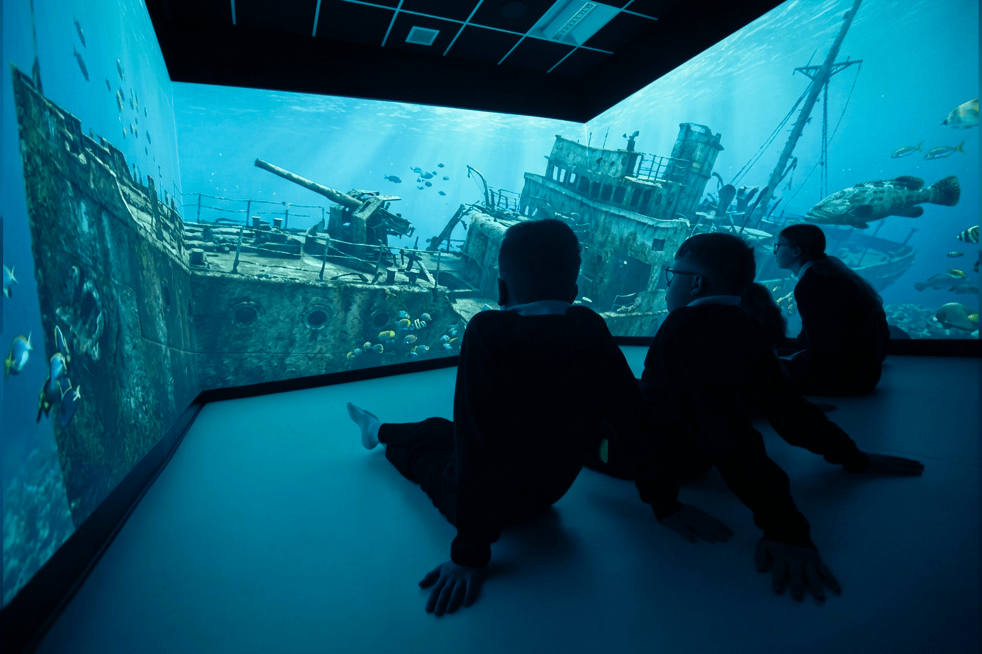 Three individuals seated in front of a large screen displaying an image of a ship.